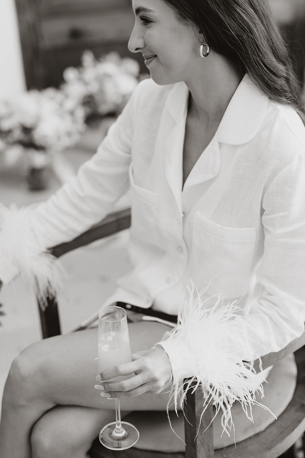 Black and white portrait of person in white jacket holding champagne glass with feather detail.