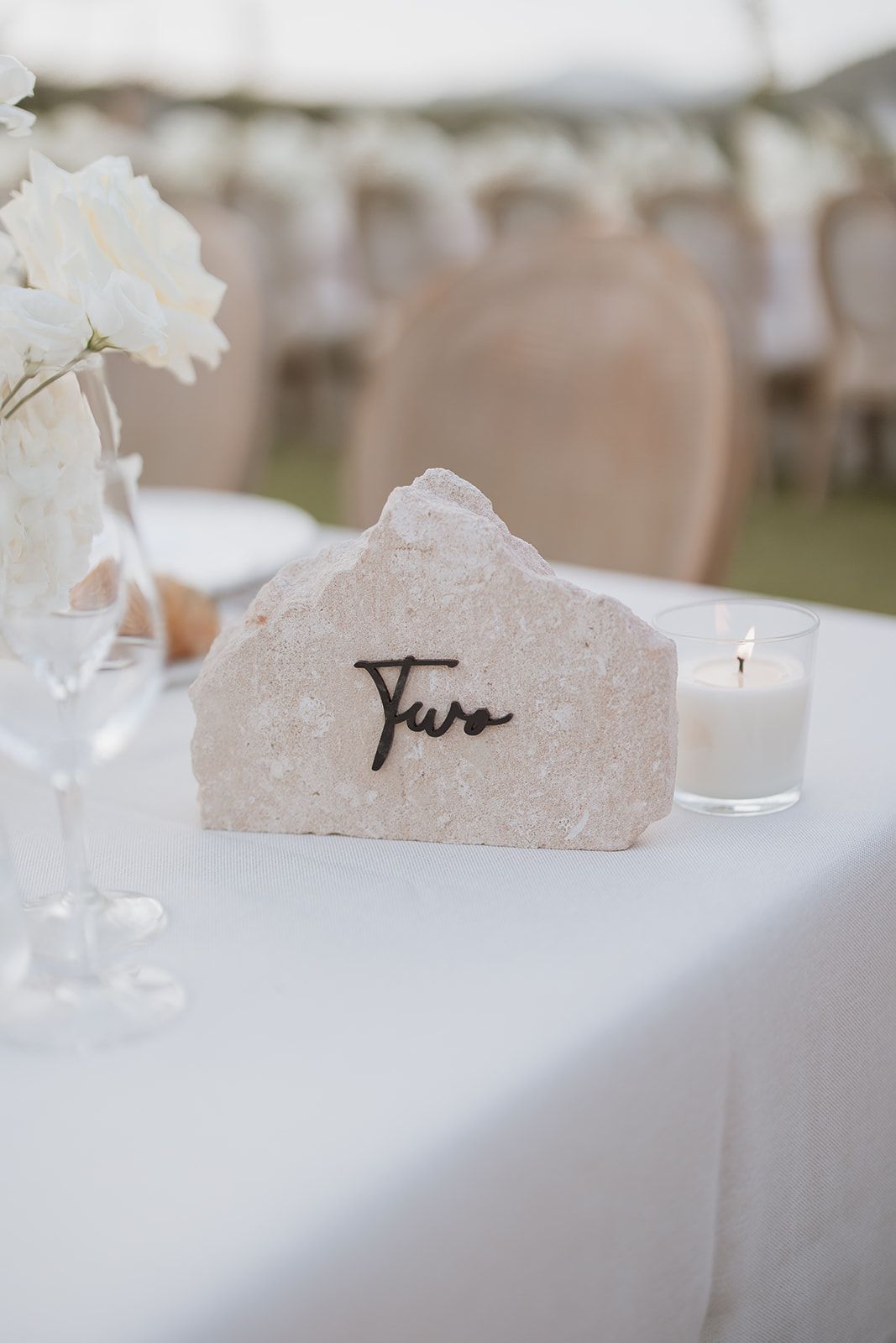 Minimalist wedding table decor featuring a stone place card holder with 'Two' written in script.