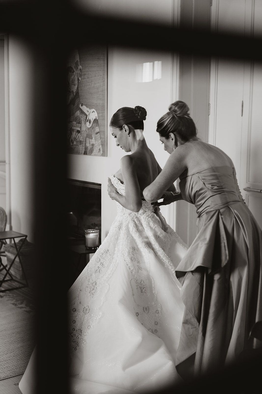 Black and white photo of wedding dress preparations through doorway.