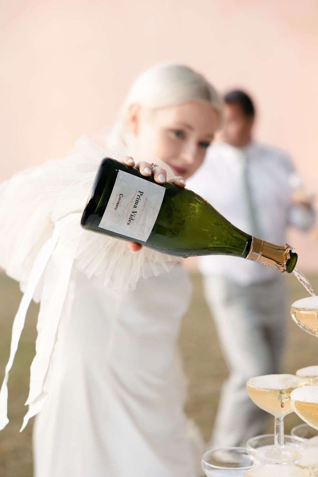 Pouring champagne into classic coupe glasses at elegant outdoor reception.