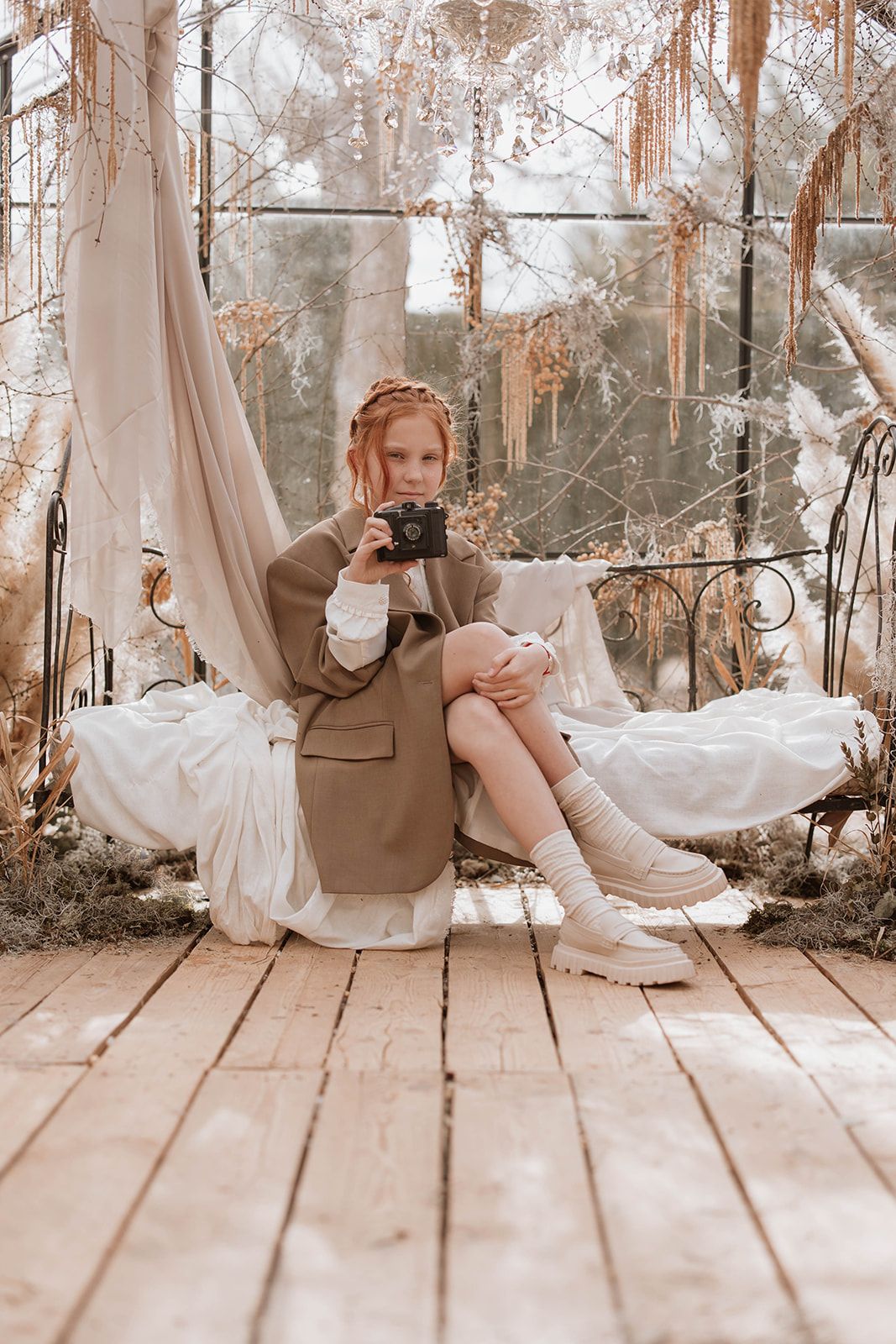 Lifestyle photo of a person with camera sitting on swing in dreamy greenhouse setting.