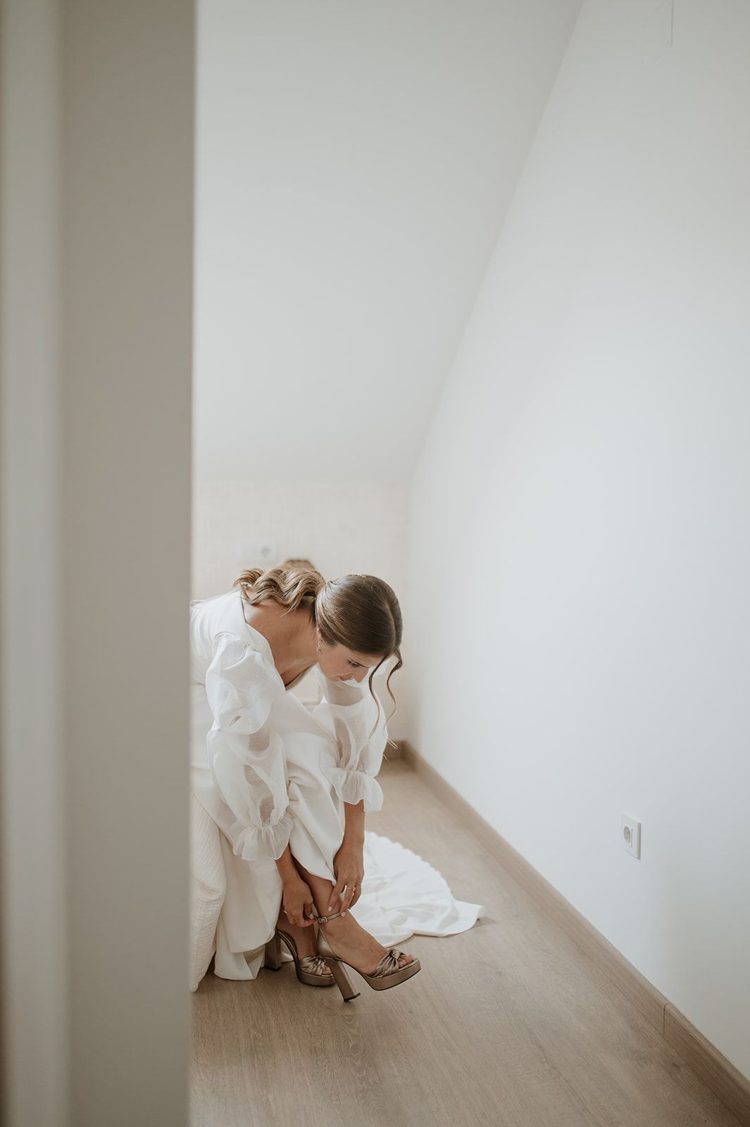 Wedding preparation moment showing white dress and shoes against light wooden floor.