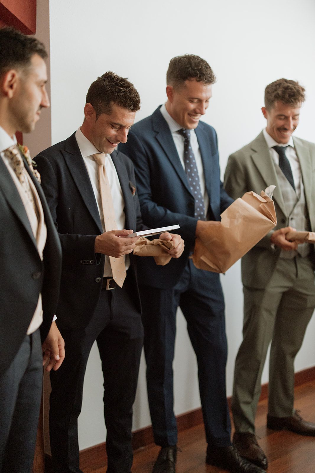 A group of groomsmen opening gifts together while wearing formal suits.