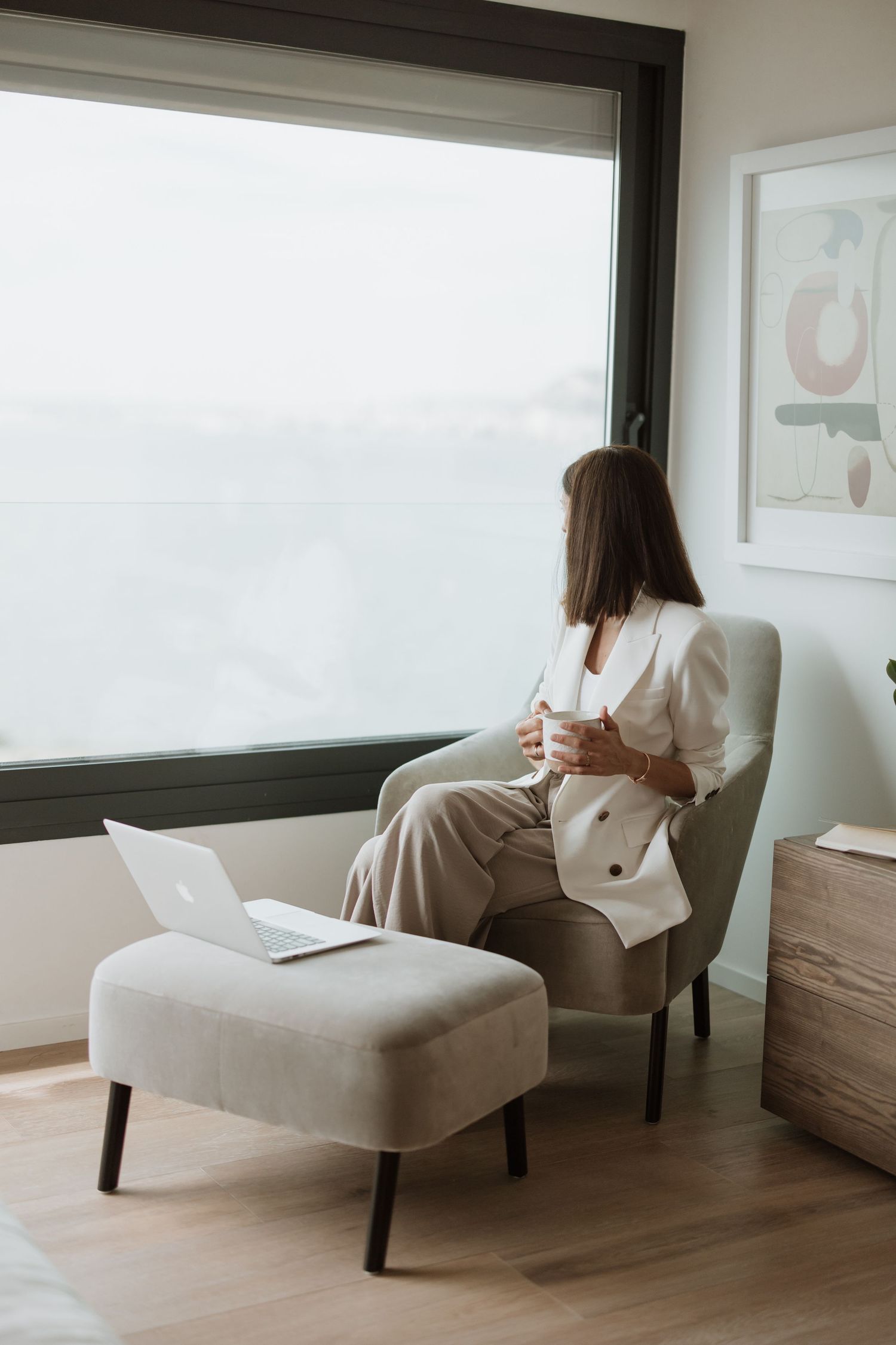 Elegant minimal home office setting with a beige chaise lounge against white walls and large windows.