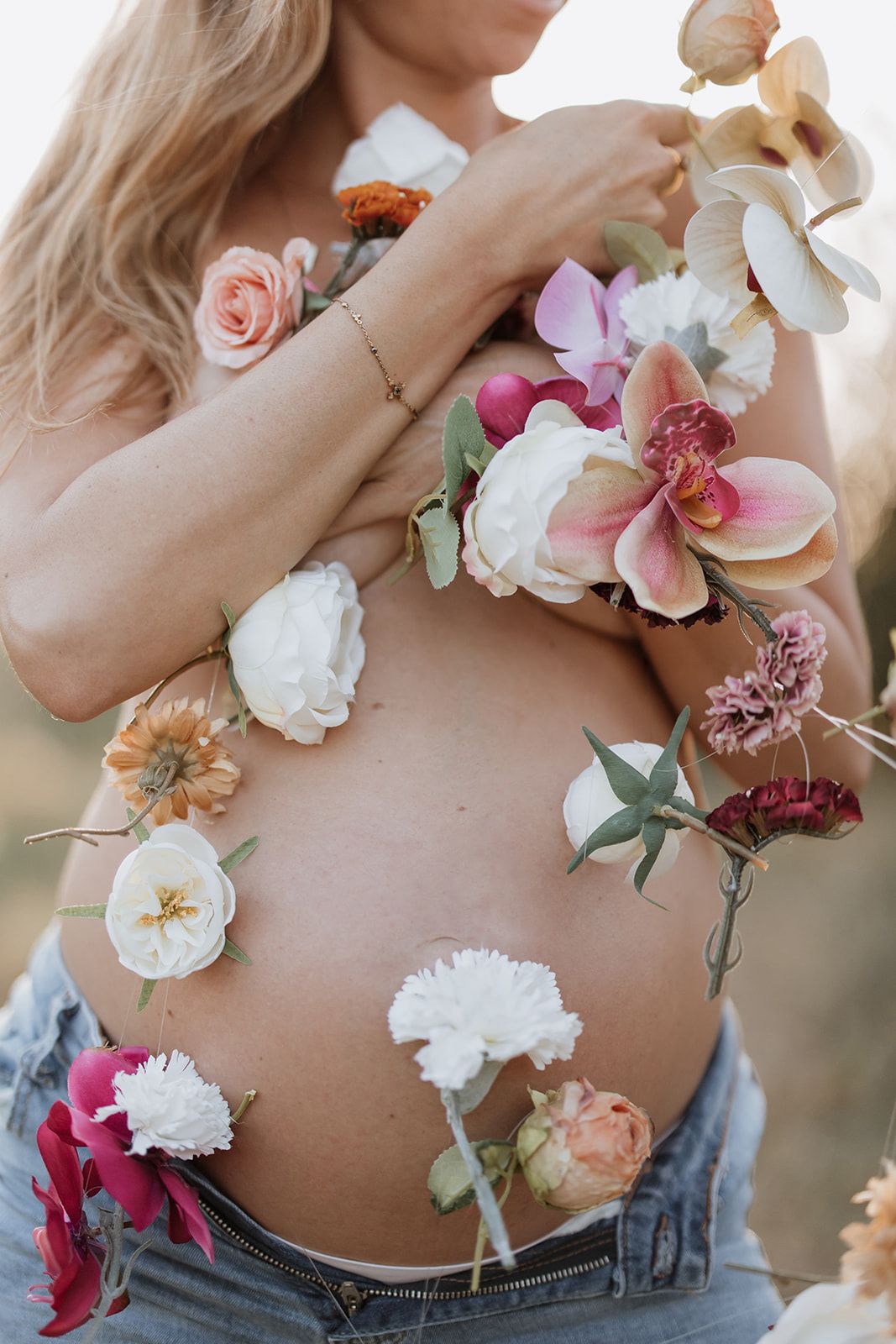 A close-up maternity photo showing pink and white flowers decorating a pregnant belly.
