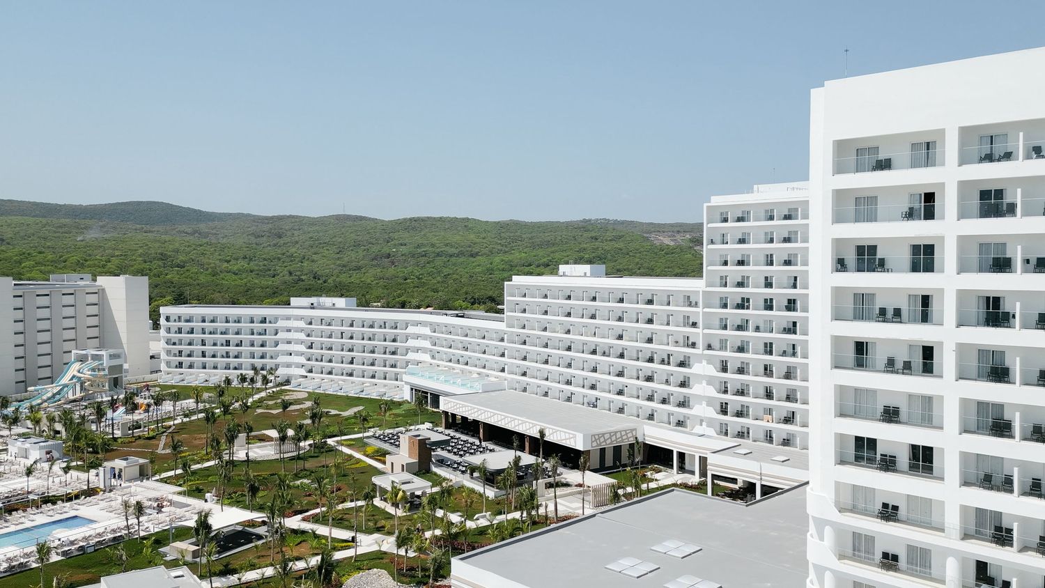 White modern hotel buildings with balconies overlooking tropical landscaping and mountains in the background.