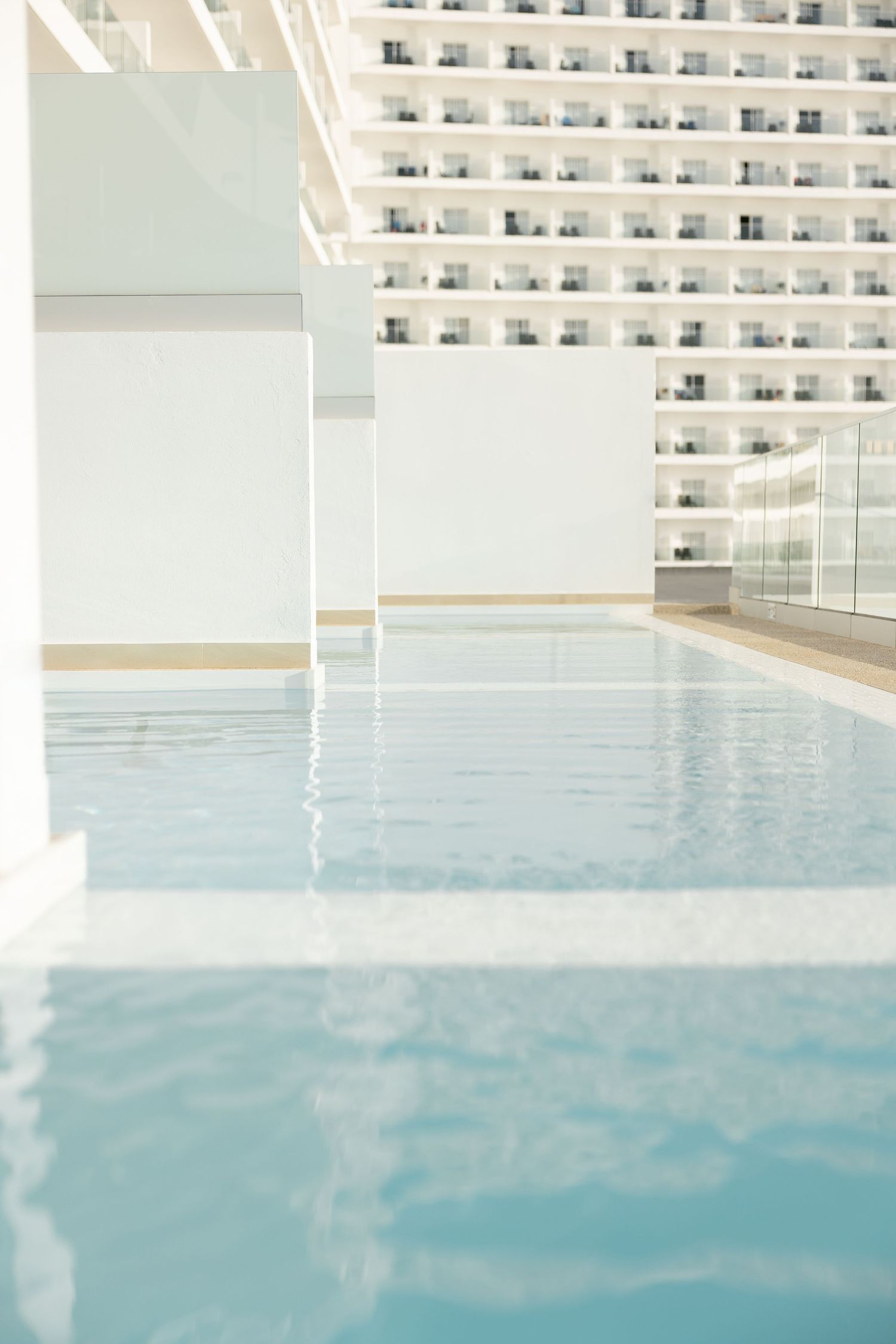 Pristine infinity pool reflecting white modern hotel architecture in calm water.