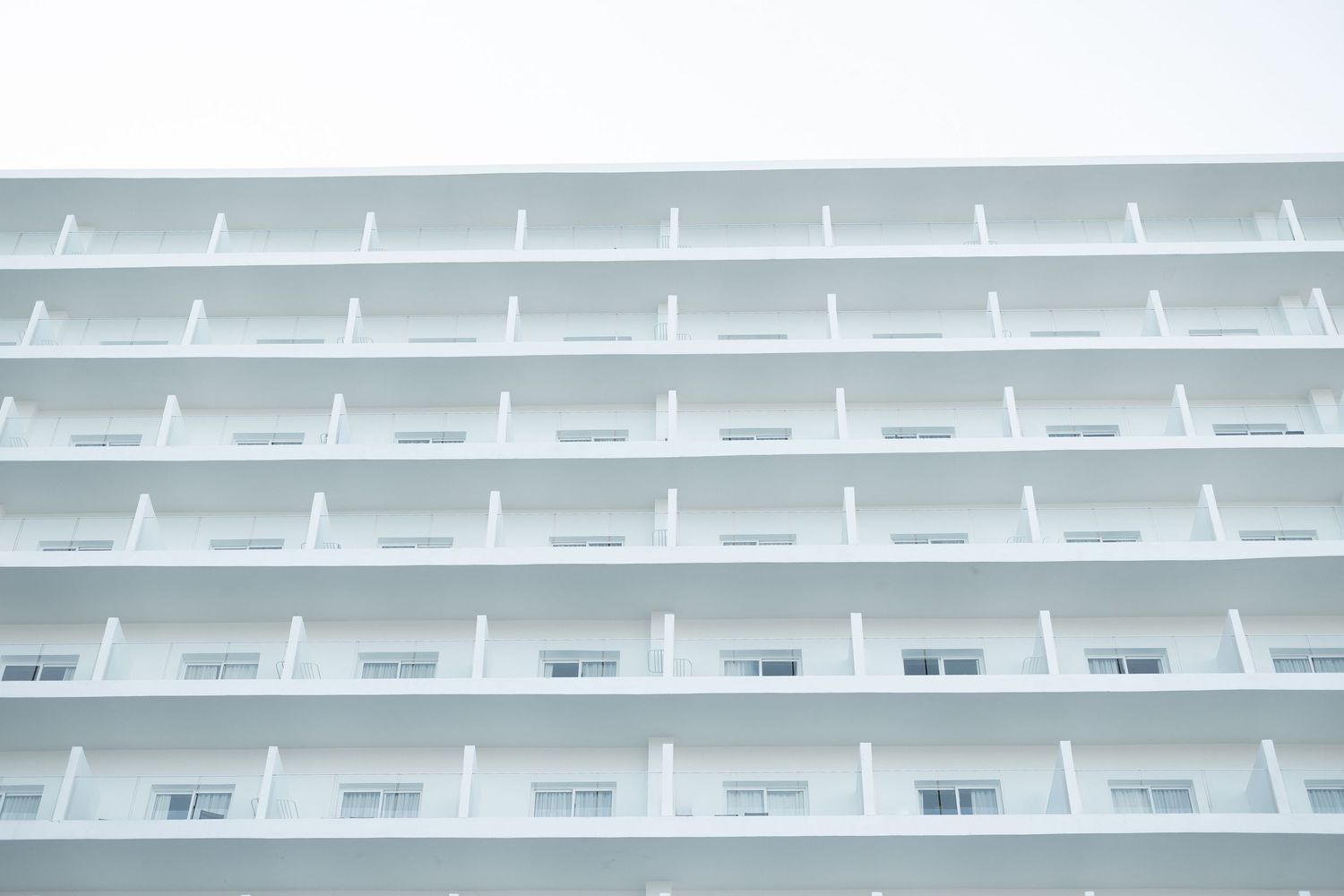 White modern hotel building facade with repeating balcony pattern against clear sky.