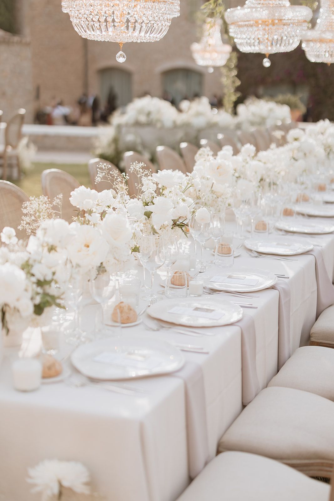White wedding reception tablescape with crystal chandeliers and delicate floral arrangements.