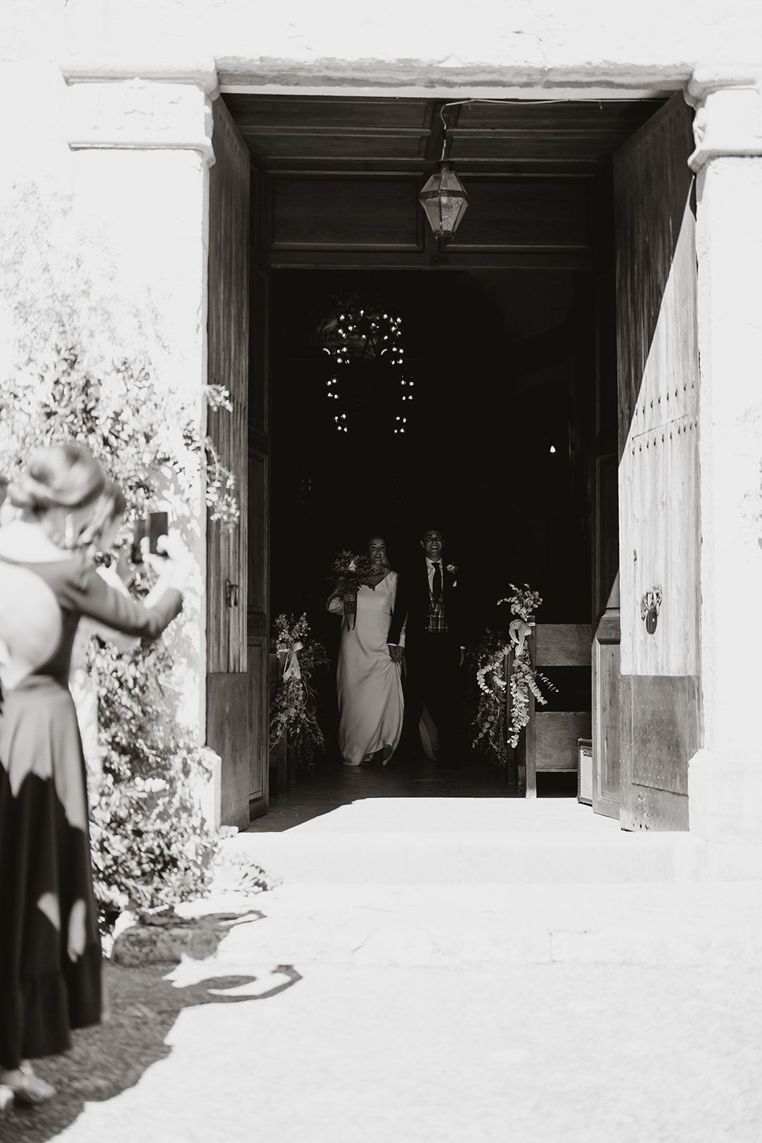 A black and white photo of newlyweds exiting through a decorated church doorway.