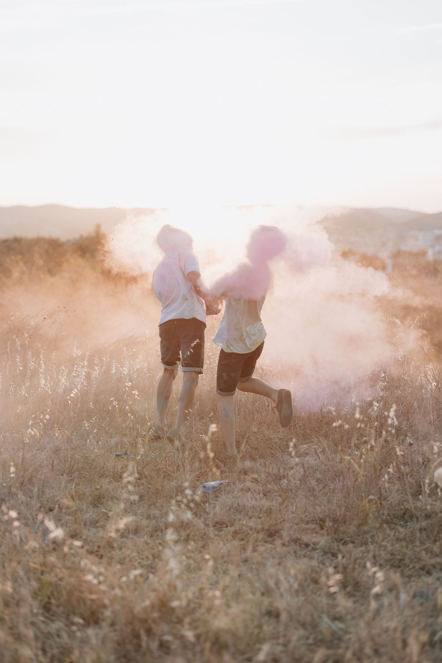 Two people running through a misty field at sunset with golden light creating a dreamy atmosphere.