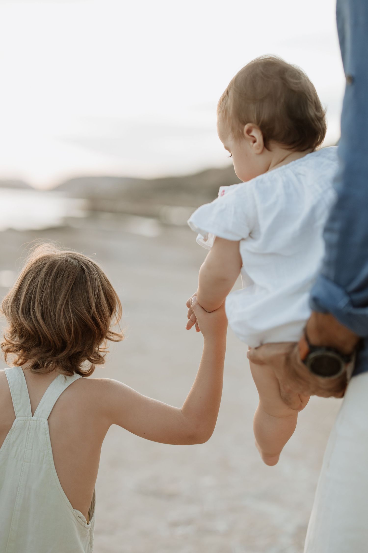 Children holding hands with adults on a scenic beach during golden hour.