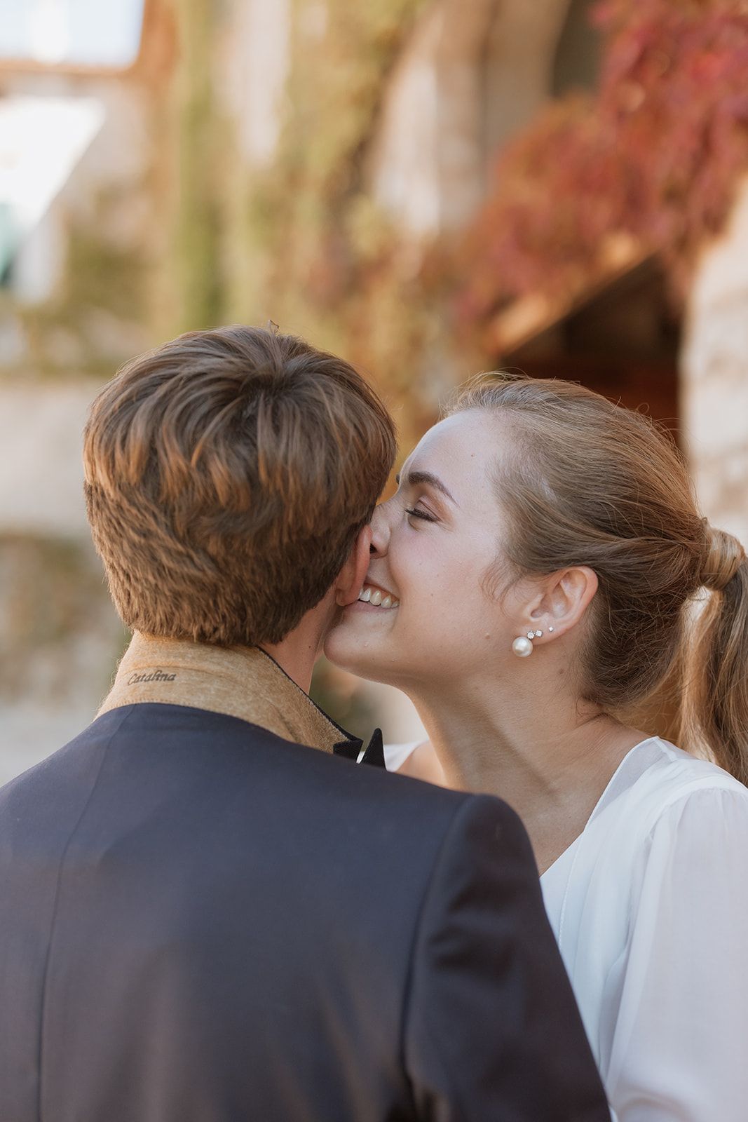 Candid moment of bride whispering to groom against blurred nature backdrop.