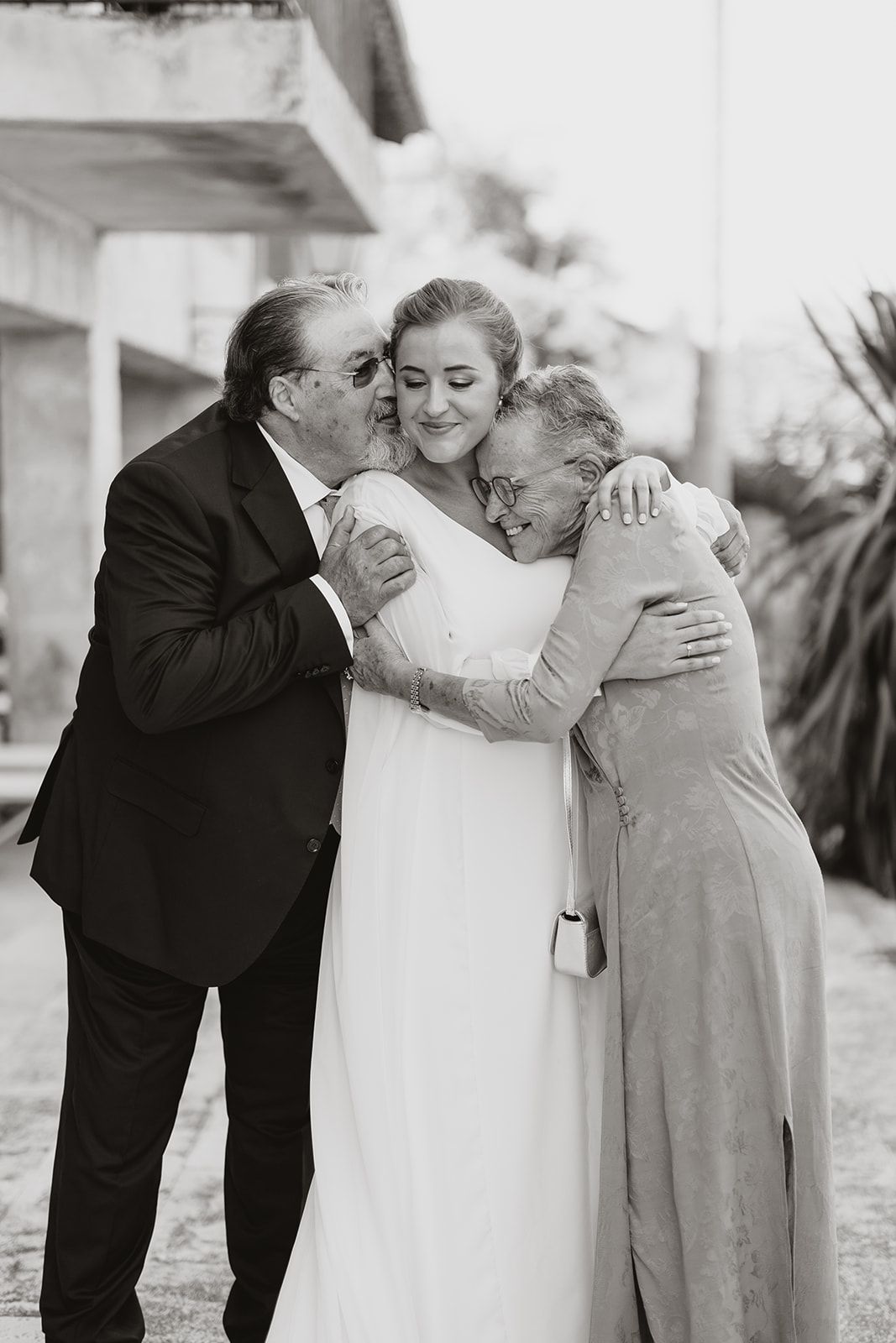 Emotional black and white photo of family members embracing bride on her wedding day.