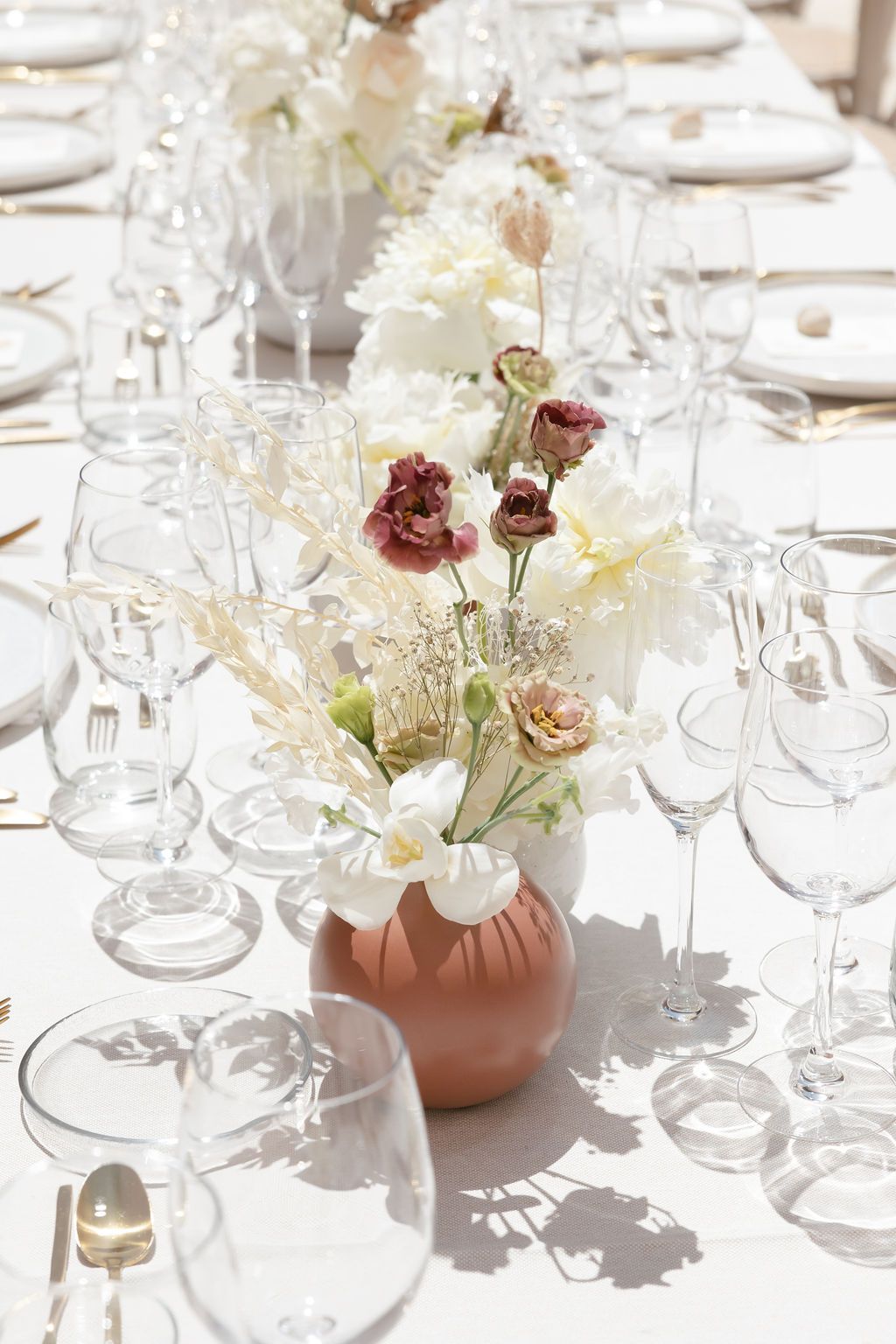 White floral centerpiece in terracotta vase surrounded by crystal glassware on formal table setting.