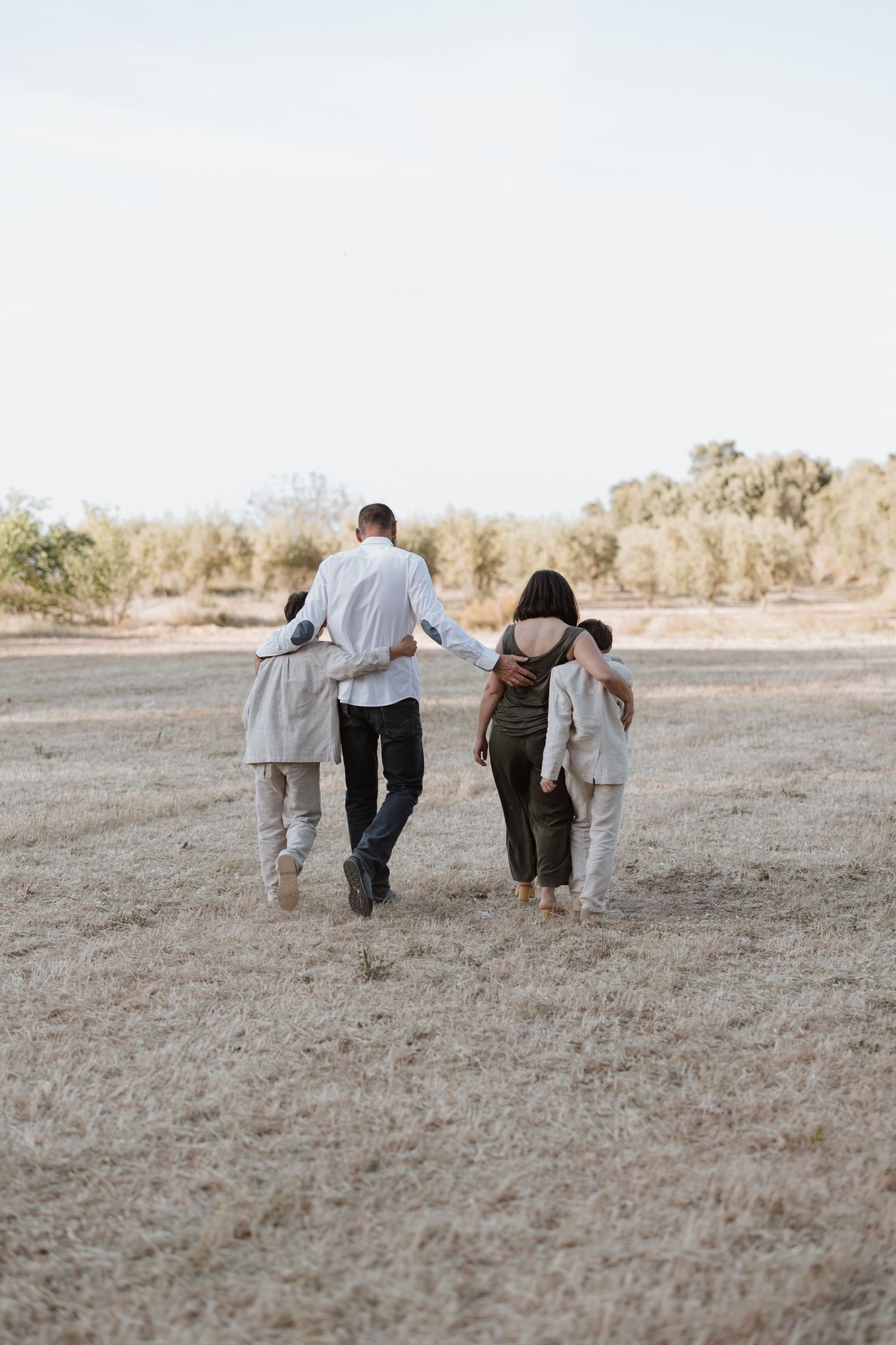 A group walks together holding each other across a dry rural field at sunset.