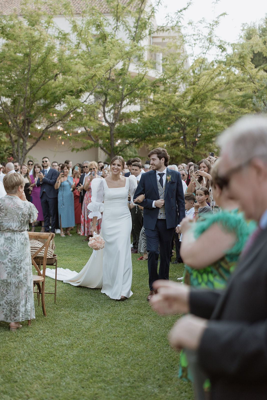 Wedding ceremony setup in a garden with rows of guests seated on wooden chairs.