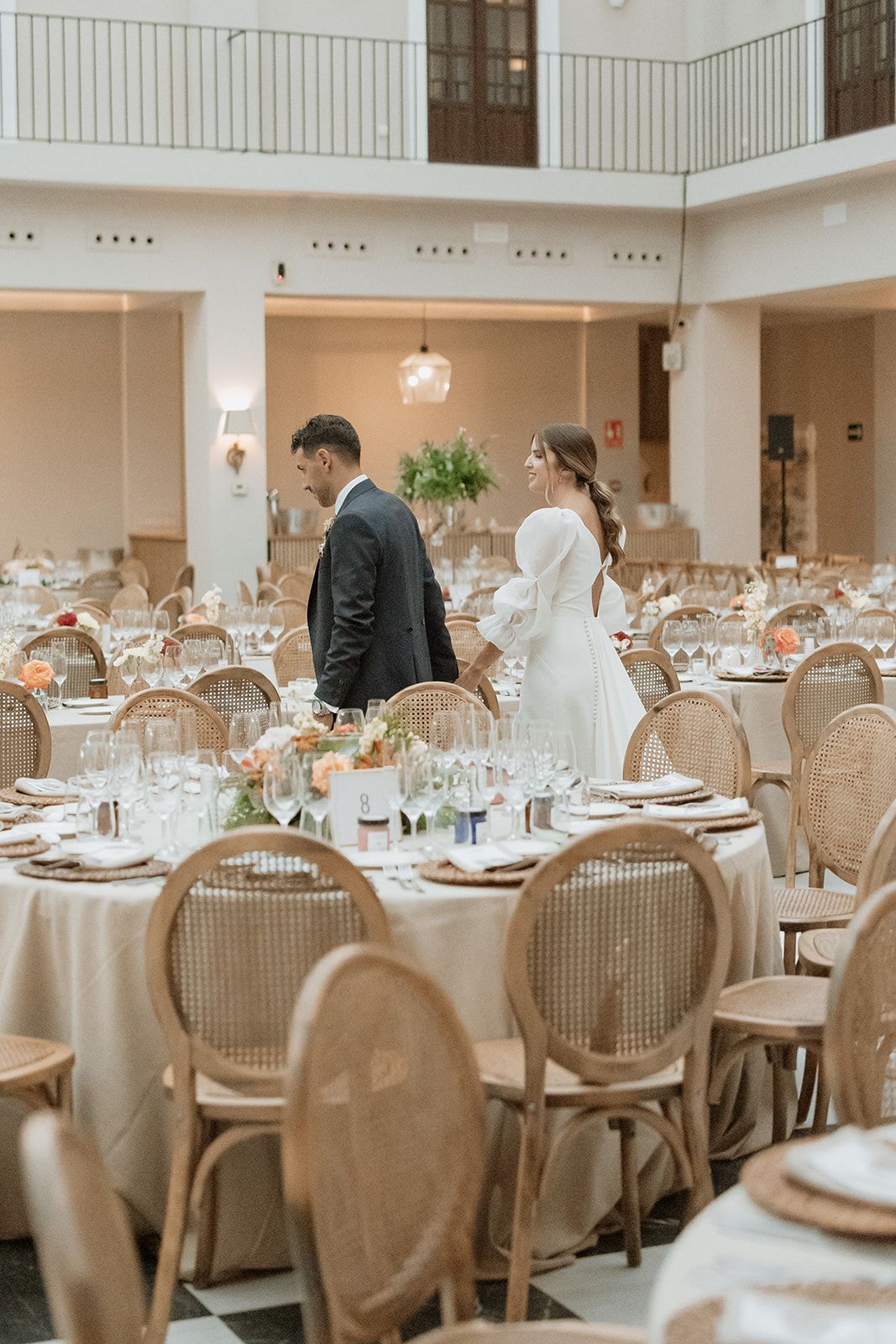 Wedding reception hall set with round tables and elegant place settings in neutral tones.