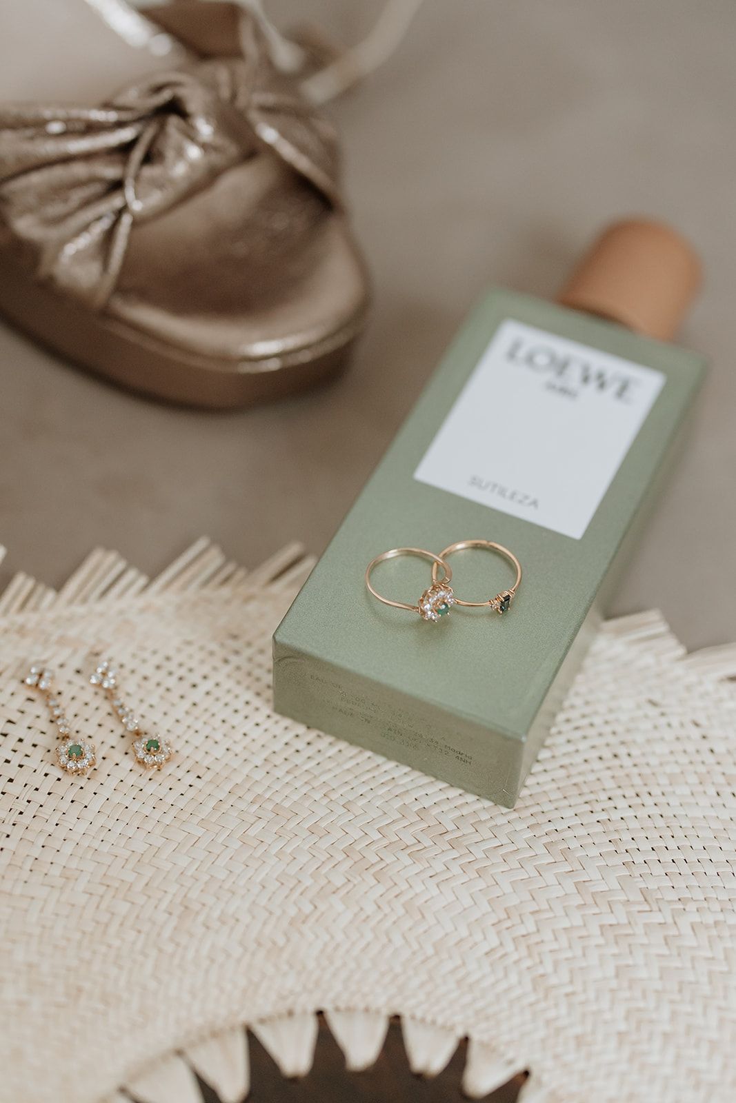 Wedding rings displayed on a mint green Loewe box with gold shoes and lace fabric.