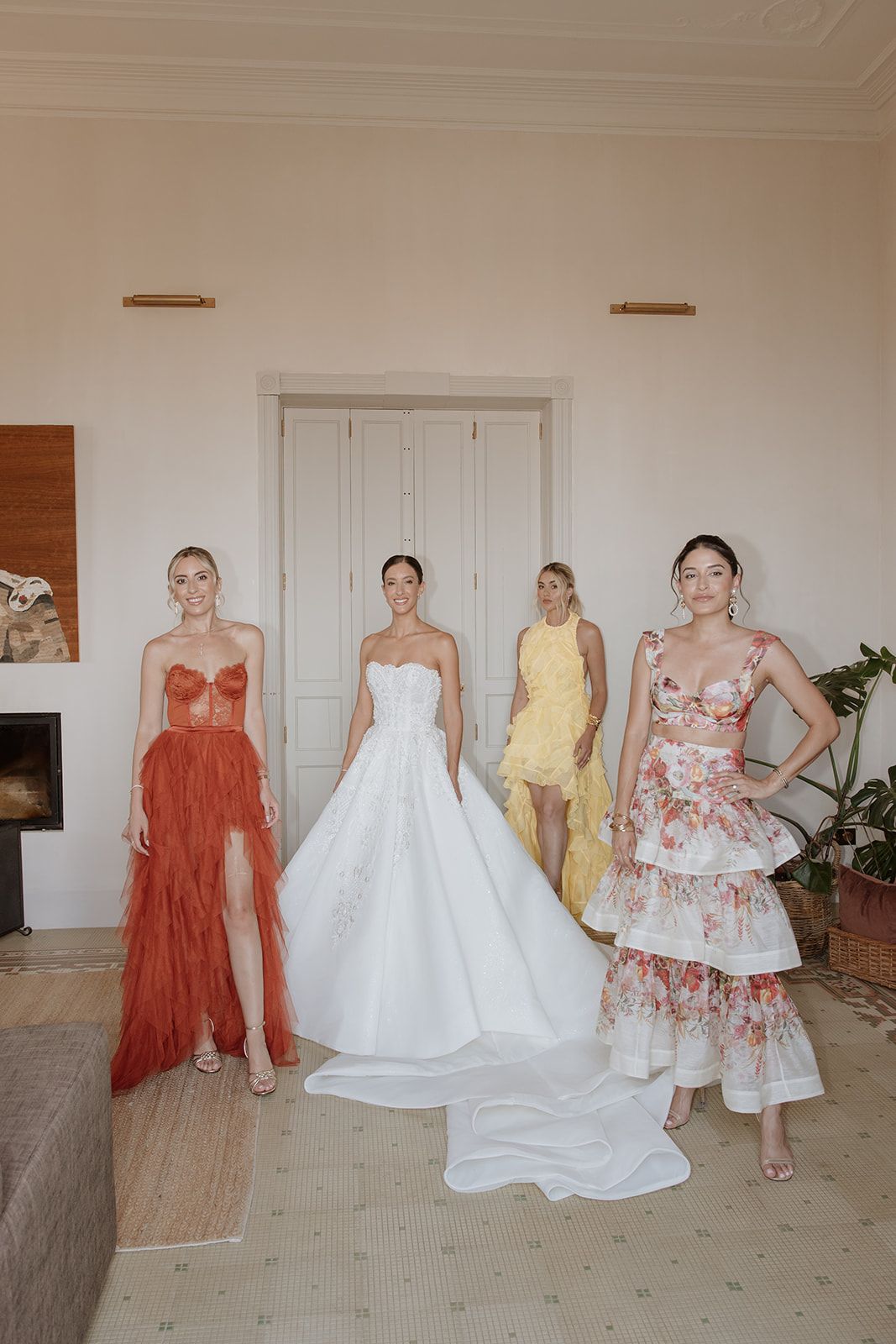 Wedding party wearing coral, white, and floral dresses posing together in an elegant room.