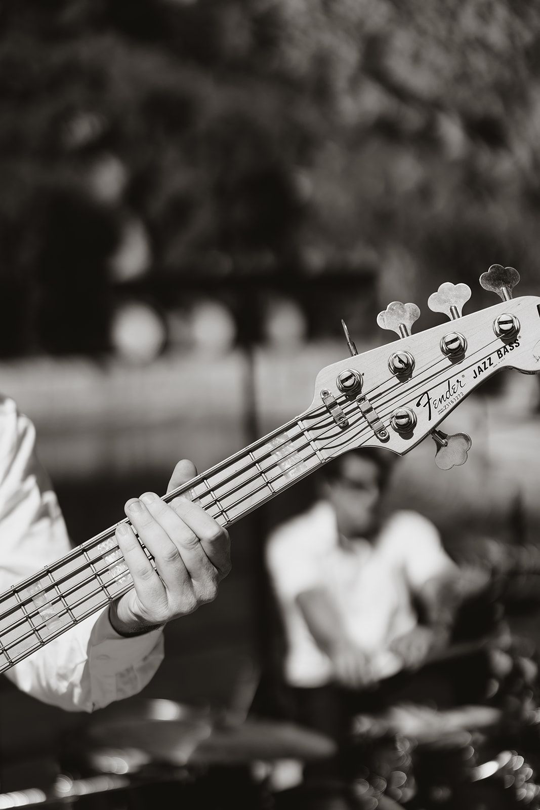 Black and white close-up of musician's hand playing bass guitar during outdoor performance.