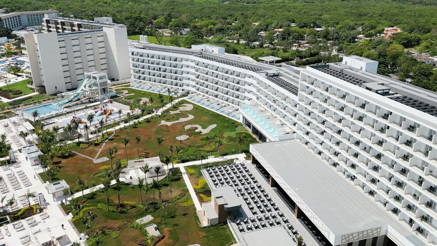 Bird's eye view of large white resort hotel complex with pools and landscaped grounds near the ocean.