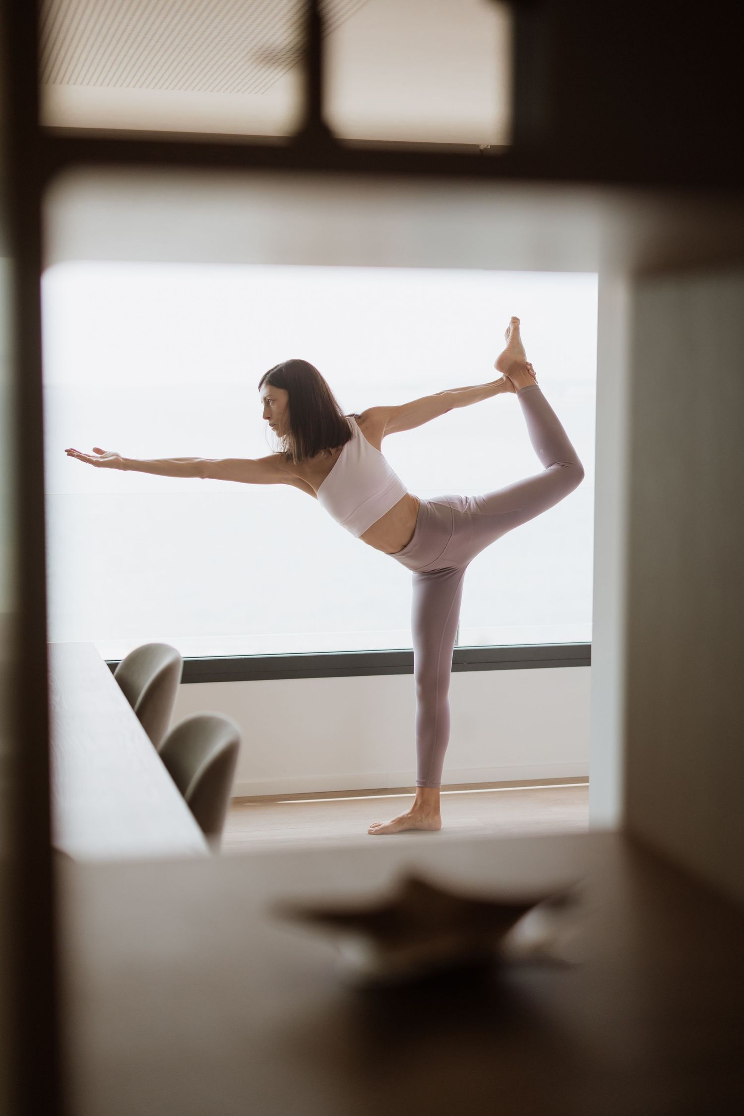 A silhouette performing a yoga dancer pose in front of a bright window.