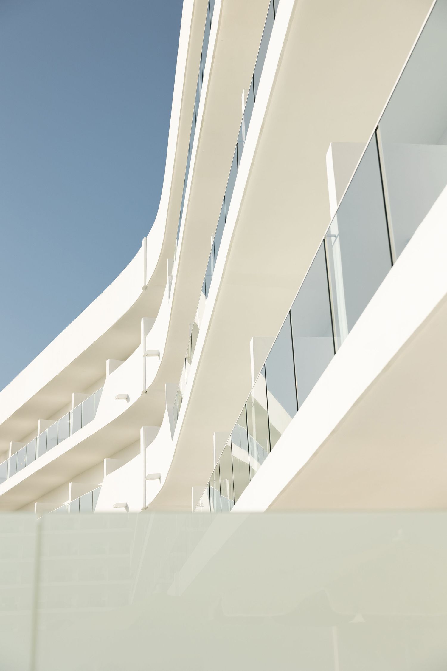 Modern white curved architecture with glass balconies against blue sky.