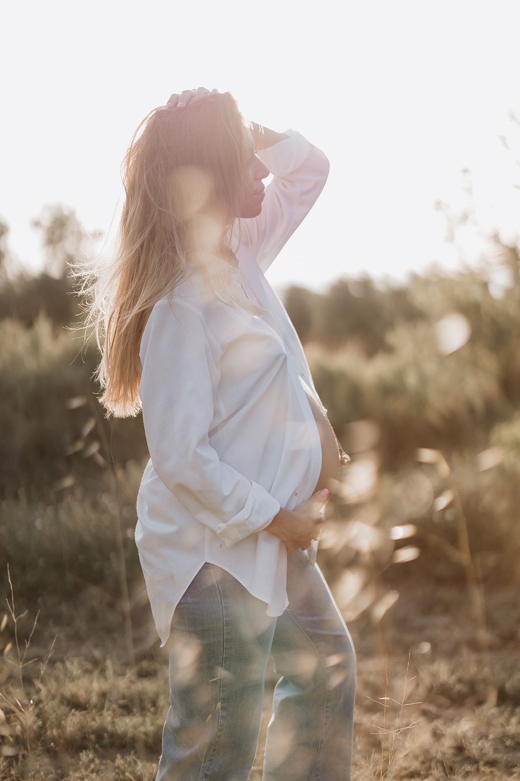 Sun-drenched maternity portrait with flowing hair and white shirt.