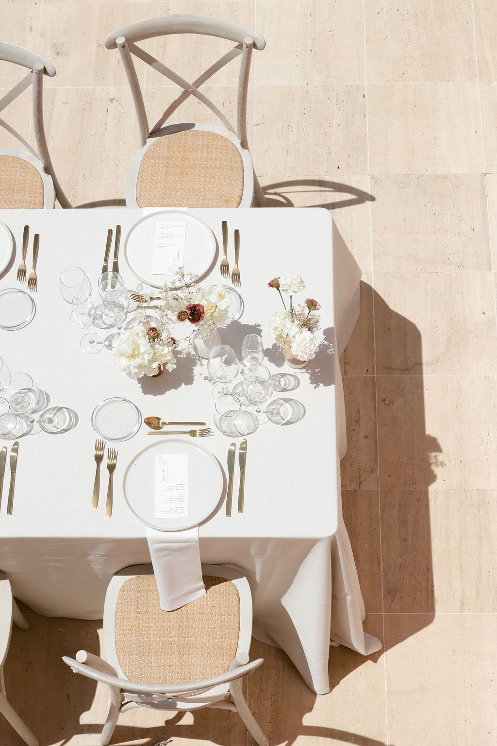 Overhead view of white table setting with crossback chairs and delicate floral centerpiece.
