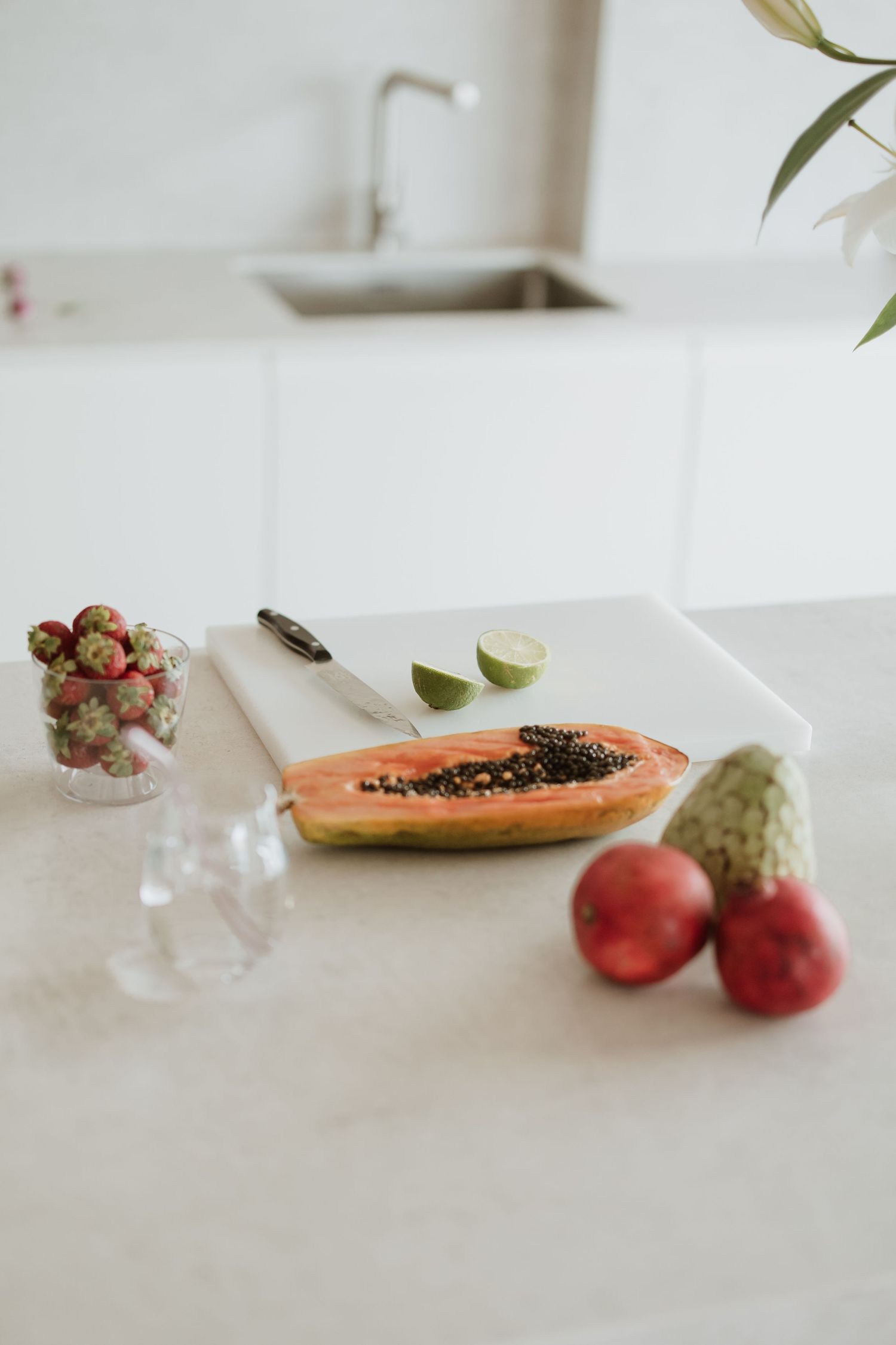 Fresh papaya, apples and fruits arranged on white kitchen counter with glass of water.