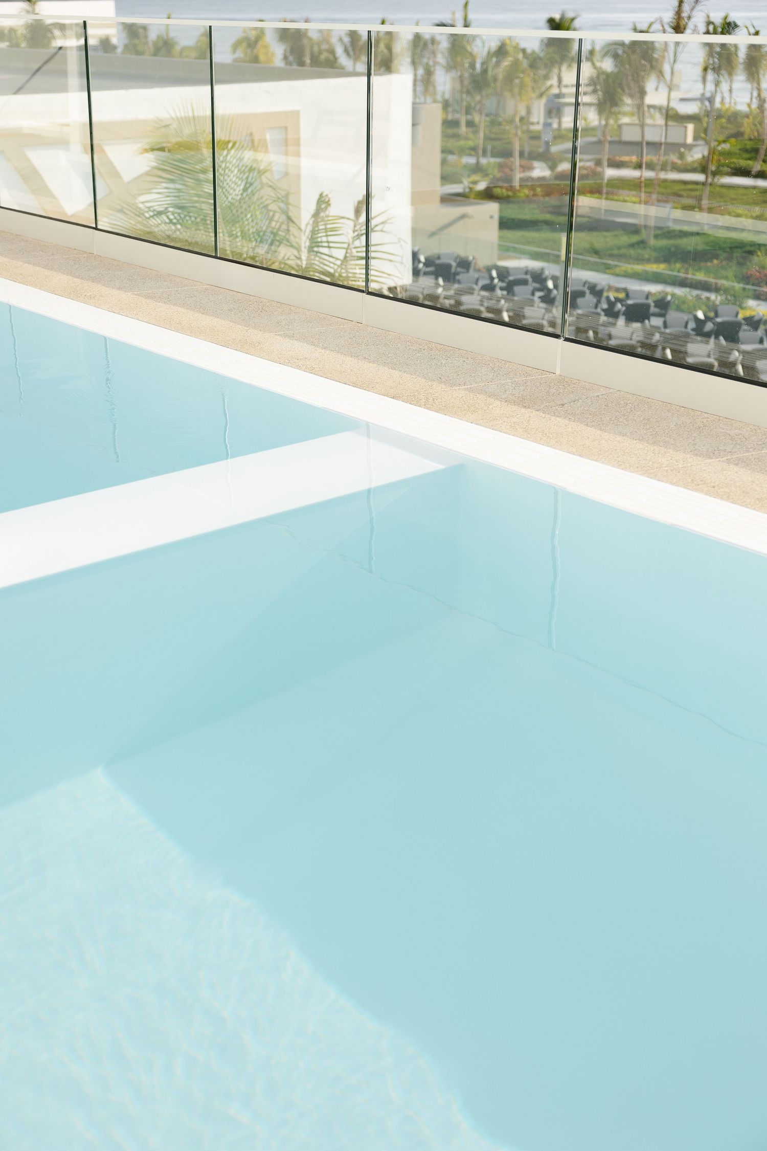 Minimalist swimming pool with turquoise water and glass railings at a modern resort property.