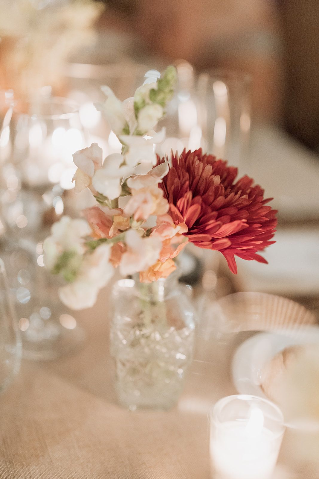 Delicate floral centerpiece with red and white flowers in small vase on wedding reception table.