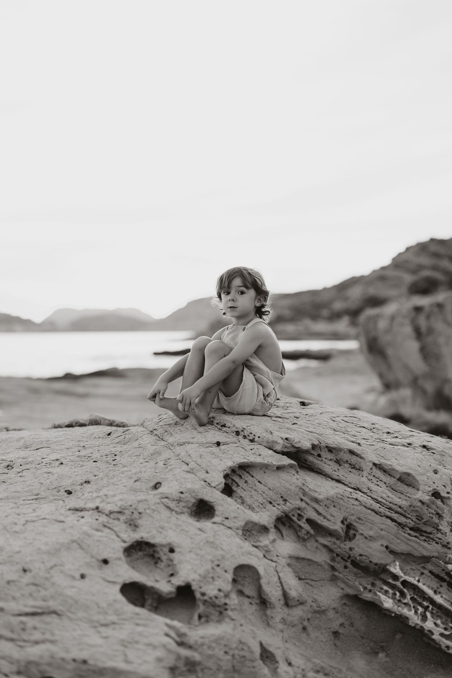 Black and white artistic photo of people lounging on textured coastal rocks.