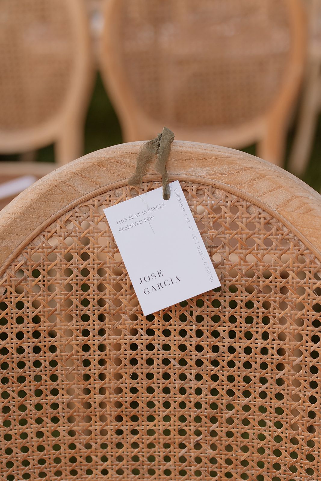Close-up of a place card attached to the back of a cane-backed wooden chair.