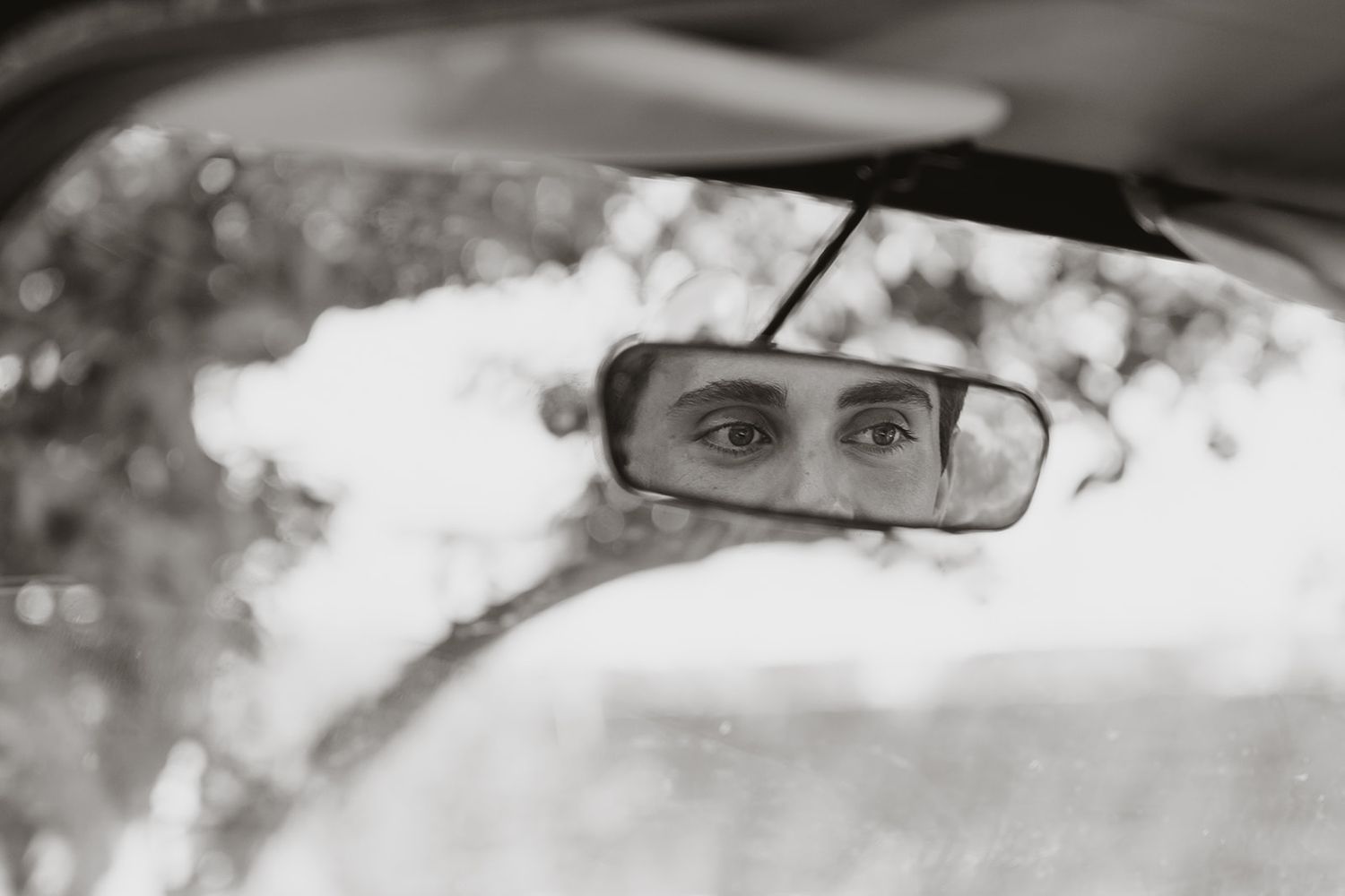 Black and white reflection in car rearview mirror showing driving perspective.