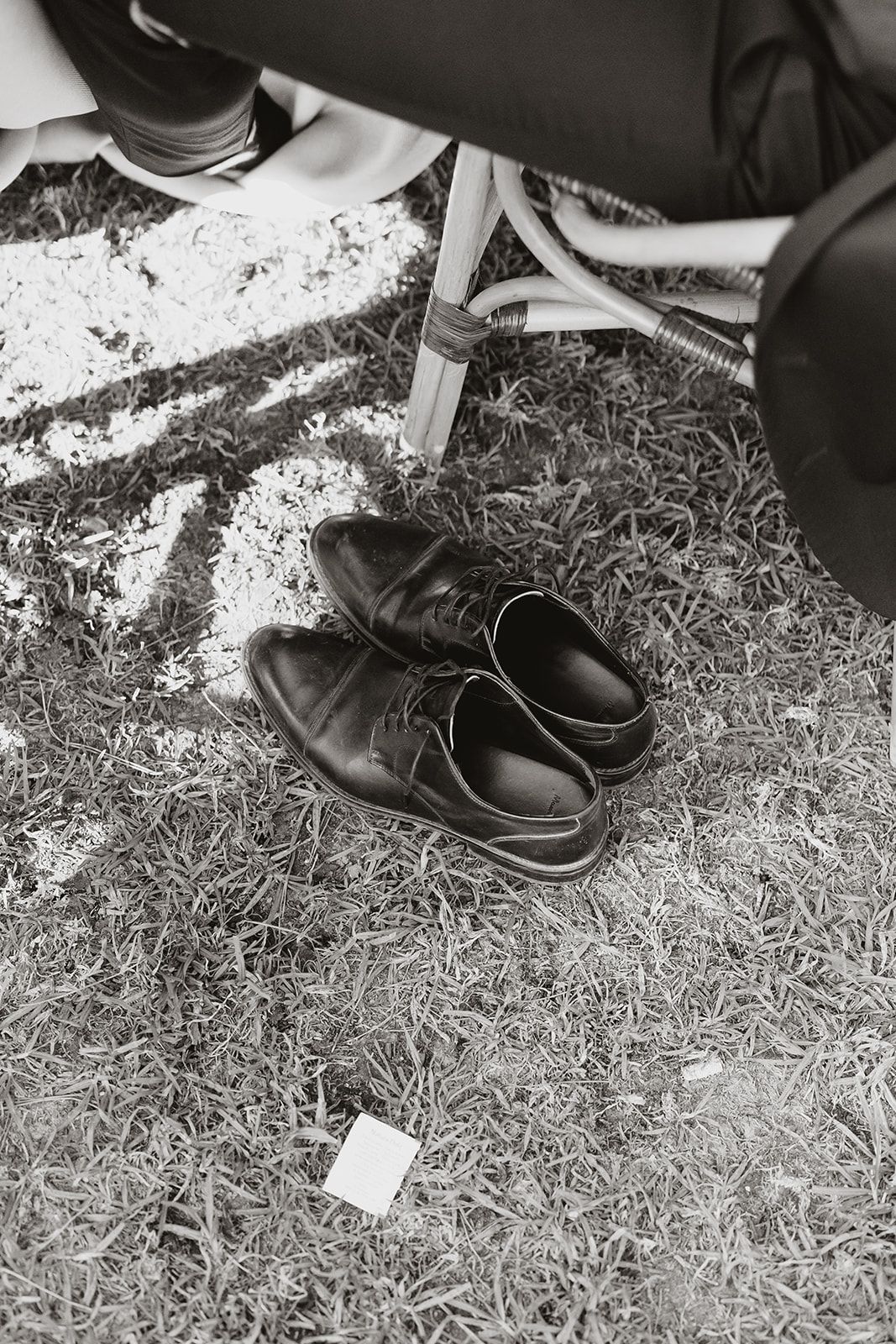 A black and white image of leather dress shoes on grass at an outdoor event.