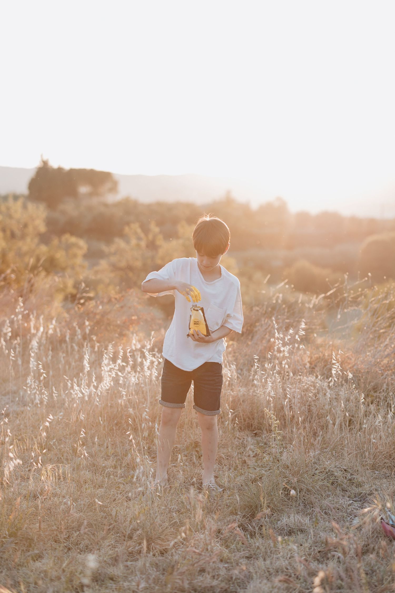 A figure in white clothing stands in a sun-drenched field of dried grass during golden hour.
