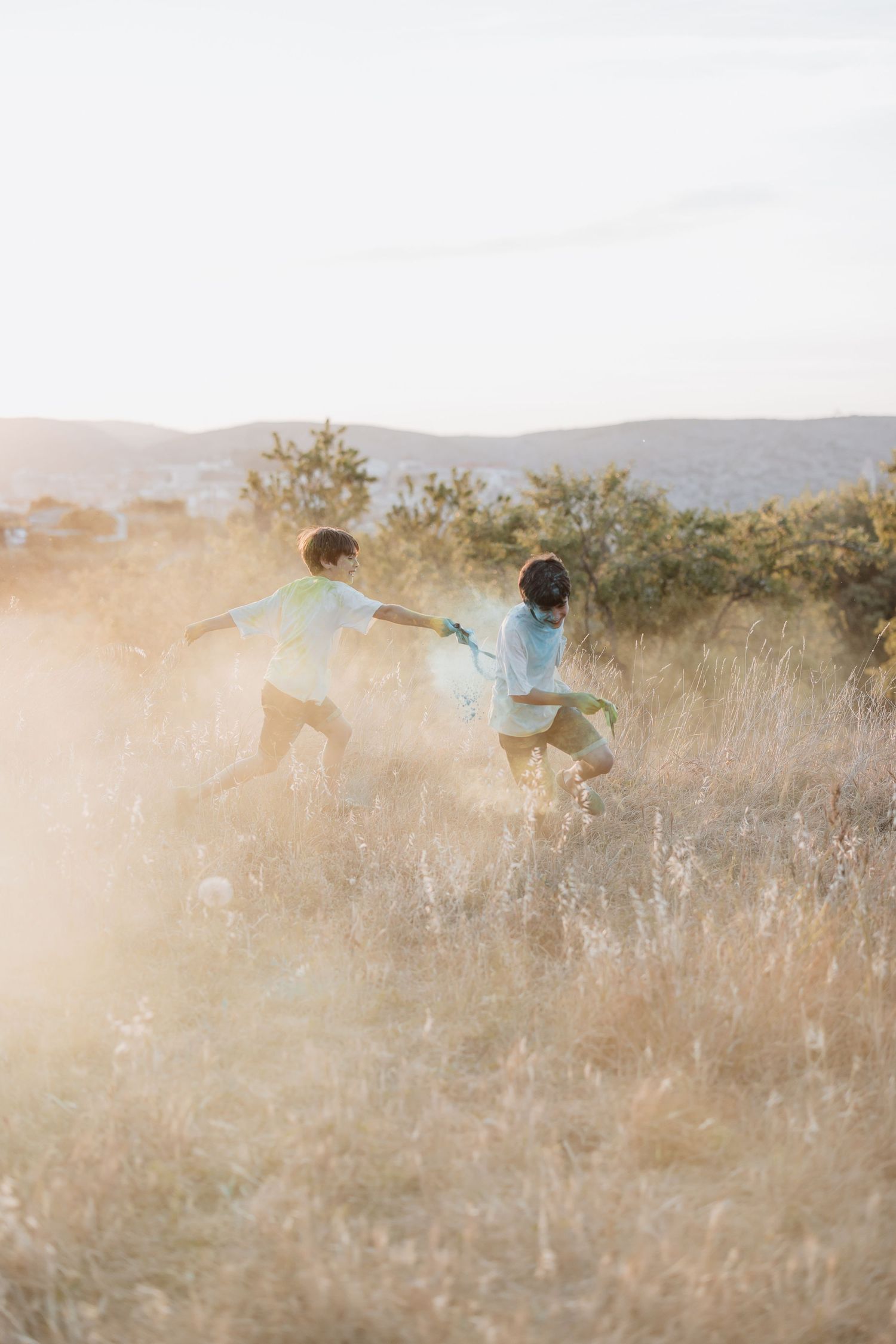 Several people run through a sunny golden field of tall grass at sunset creating a dreamy outdoor scene.
