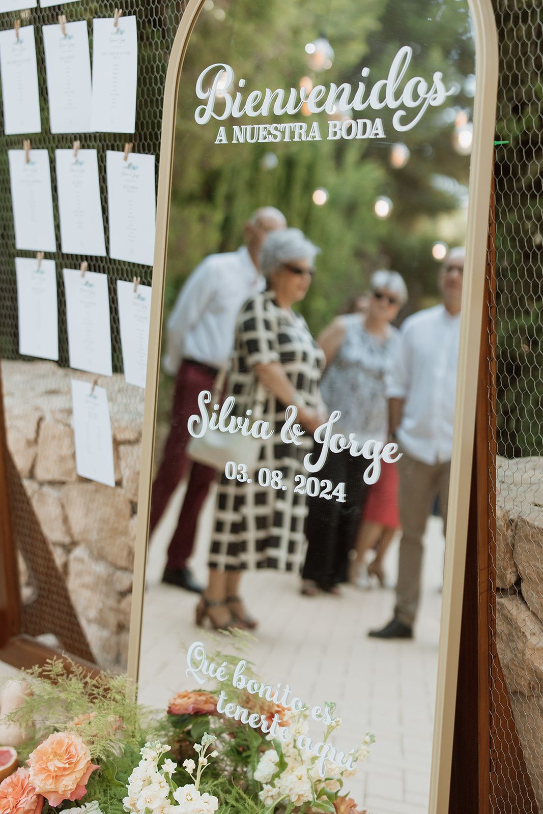 Spanish wedding welcome sign with florals and mirror design reflecting guests at a wedding.