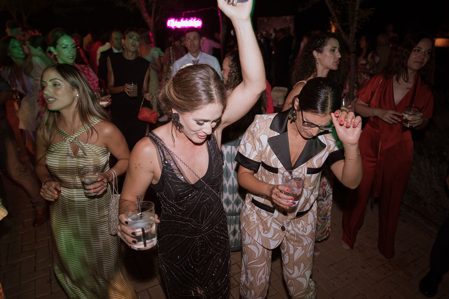 Dancing partygoers enjoying a lively celebration with drinks in hand at a nighttime event.