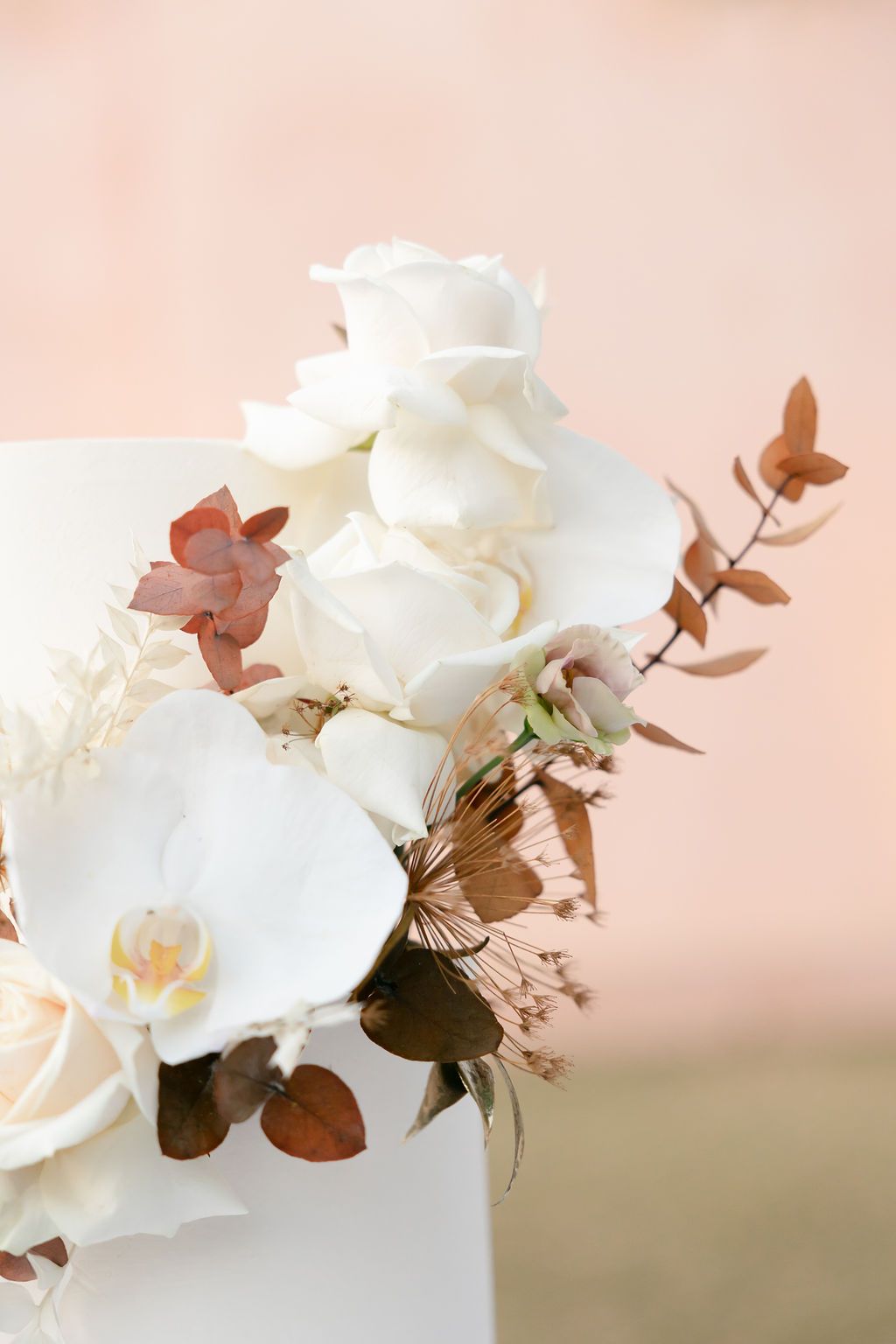 Close-up of white wedding cake decorated with orchids and copper-toned leaves.