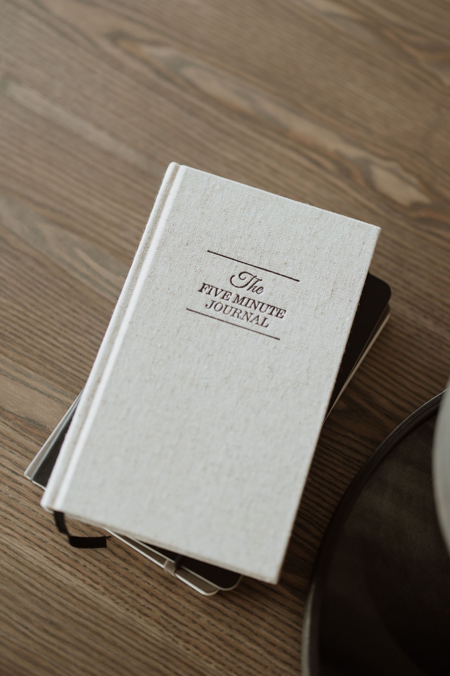 A white hardcover book titled 'The Five Minute Journal' resting on a wooden surface.