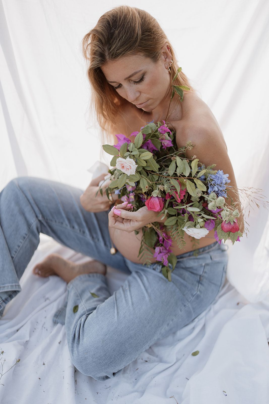 Dreamy outdoor maternity session with colorful wildflower bouquet and white fabric backdrop.