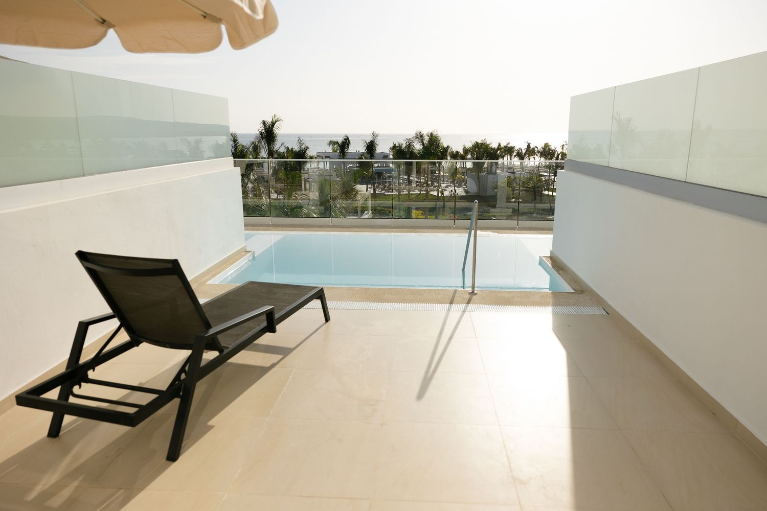 Modern lounge chair on balcony terrace with glass railing overlooking palm trees.