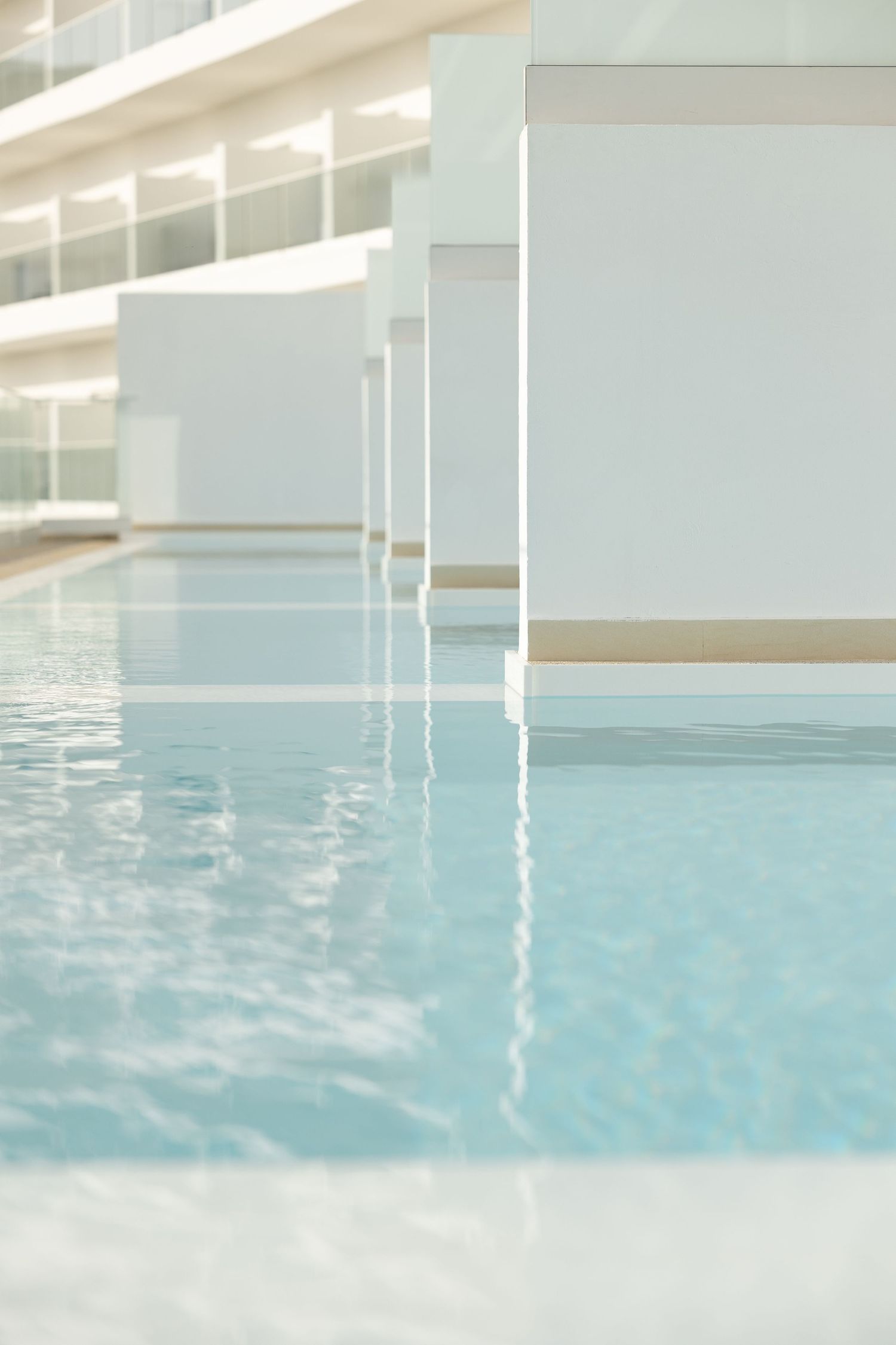 Calm turquoise swimming pool with white architectural columns and walls reflecting in the crystal clear water.