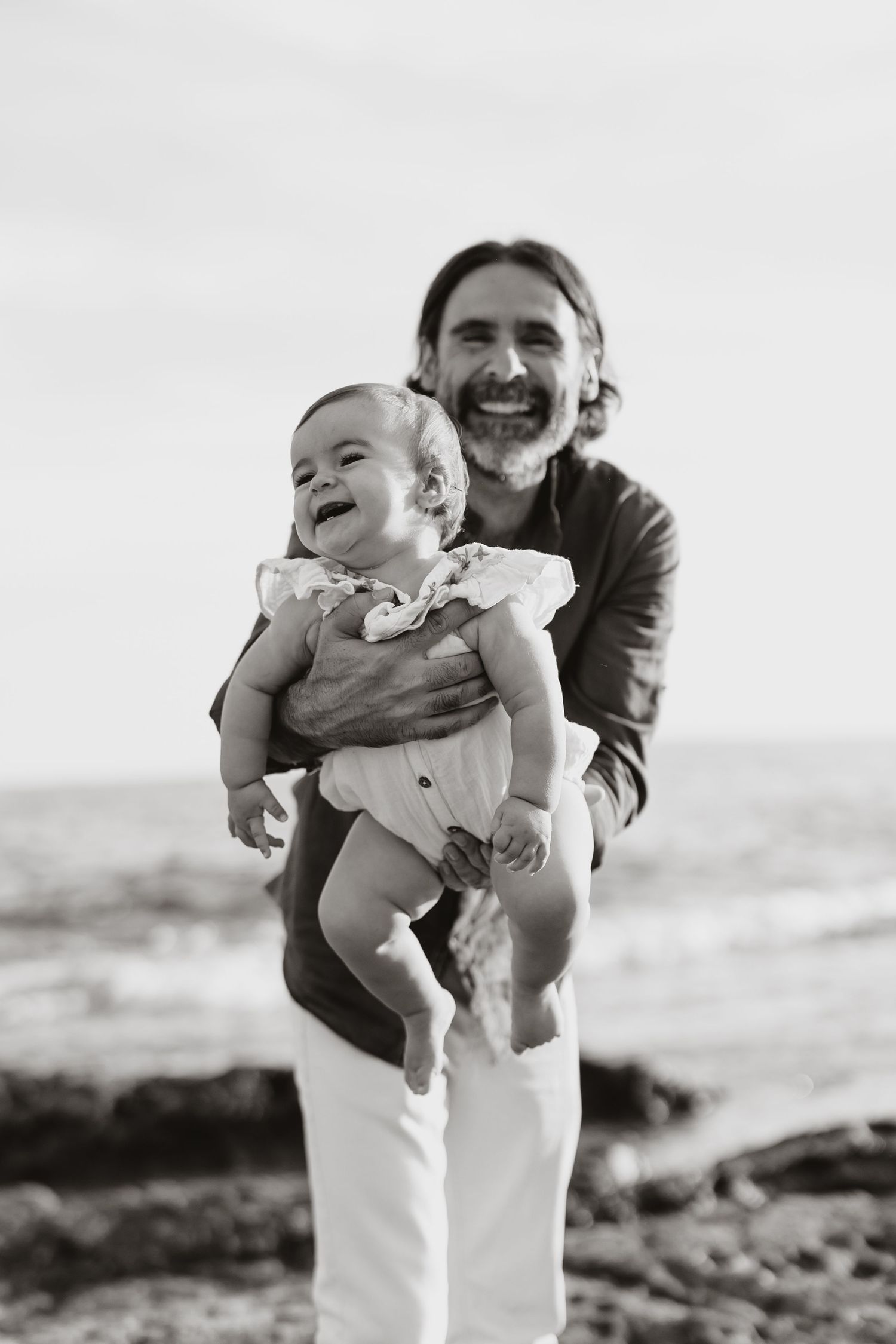 A black and white portrait of pure joy shared between adult and baby at the beach.