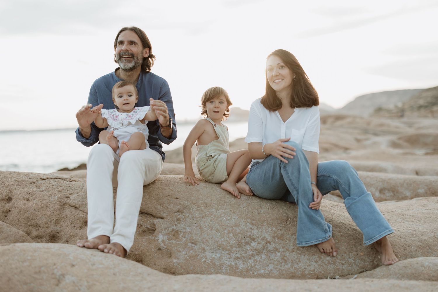 Family members interact playfully while sitting on rocky coastal terrain.