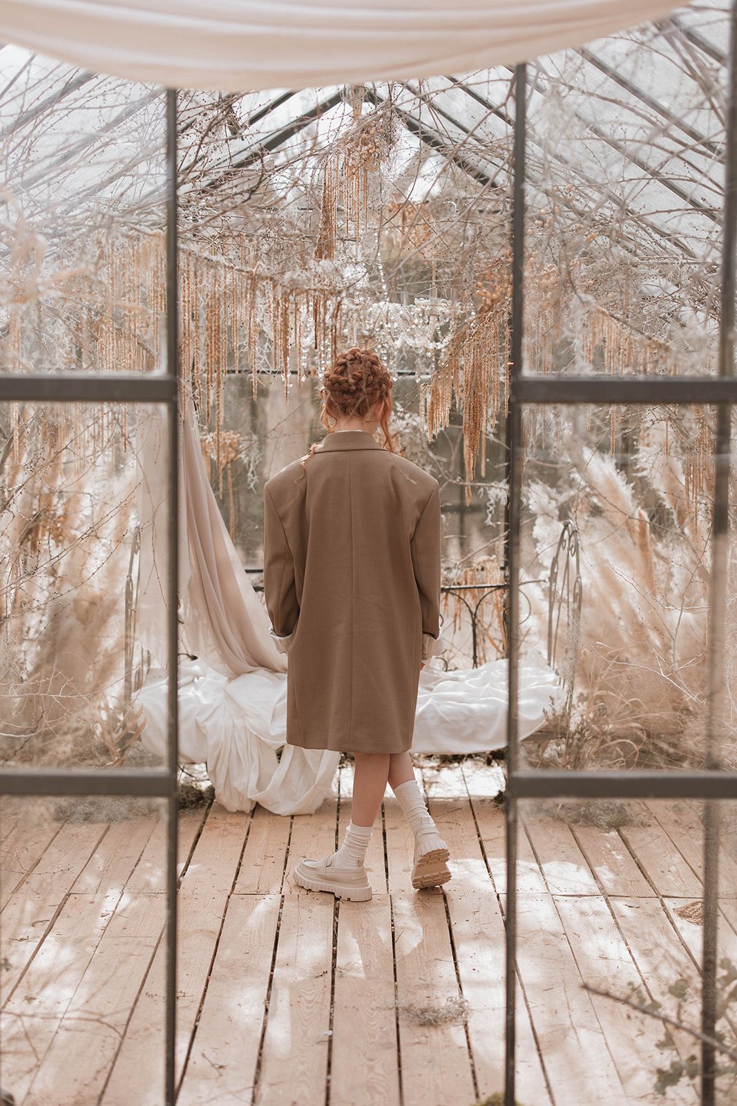 Back view of a vintage-inspired winter scene in a greenhouse with draped fabrics and soft lighting.