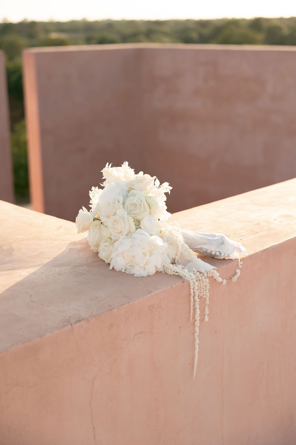 White rose wedding bouquet and accessories displayed on pink concrete ledge at sunset.